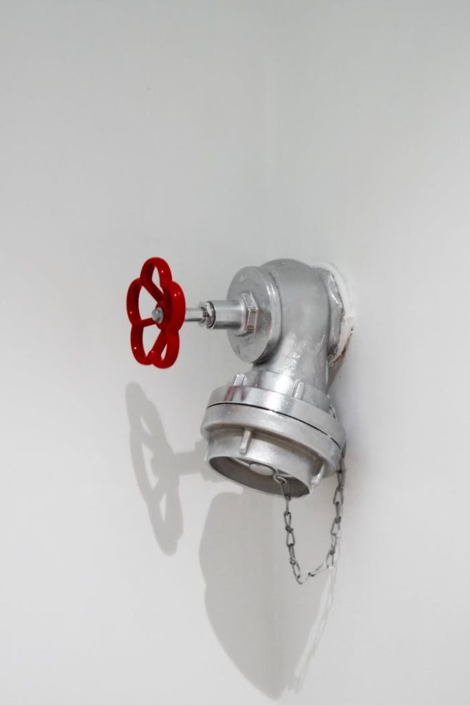 Detailed view of a silver plumbing installation with a red valve on a white wall in Eskişehir.